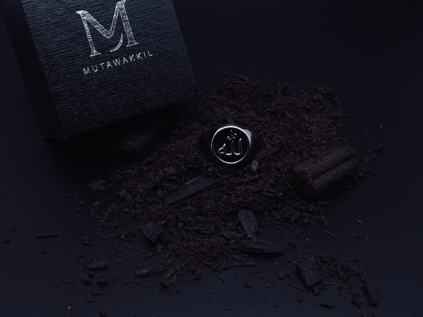 Mutawakkil Quwwah black Islamic ring engraved with Allah in Arabic calligraphy, symbol of strength, beside luxury black box.