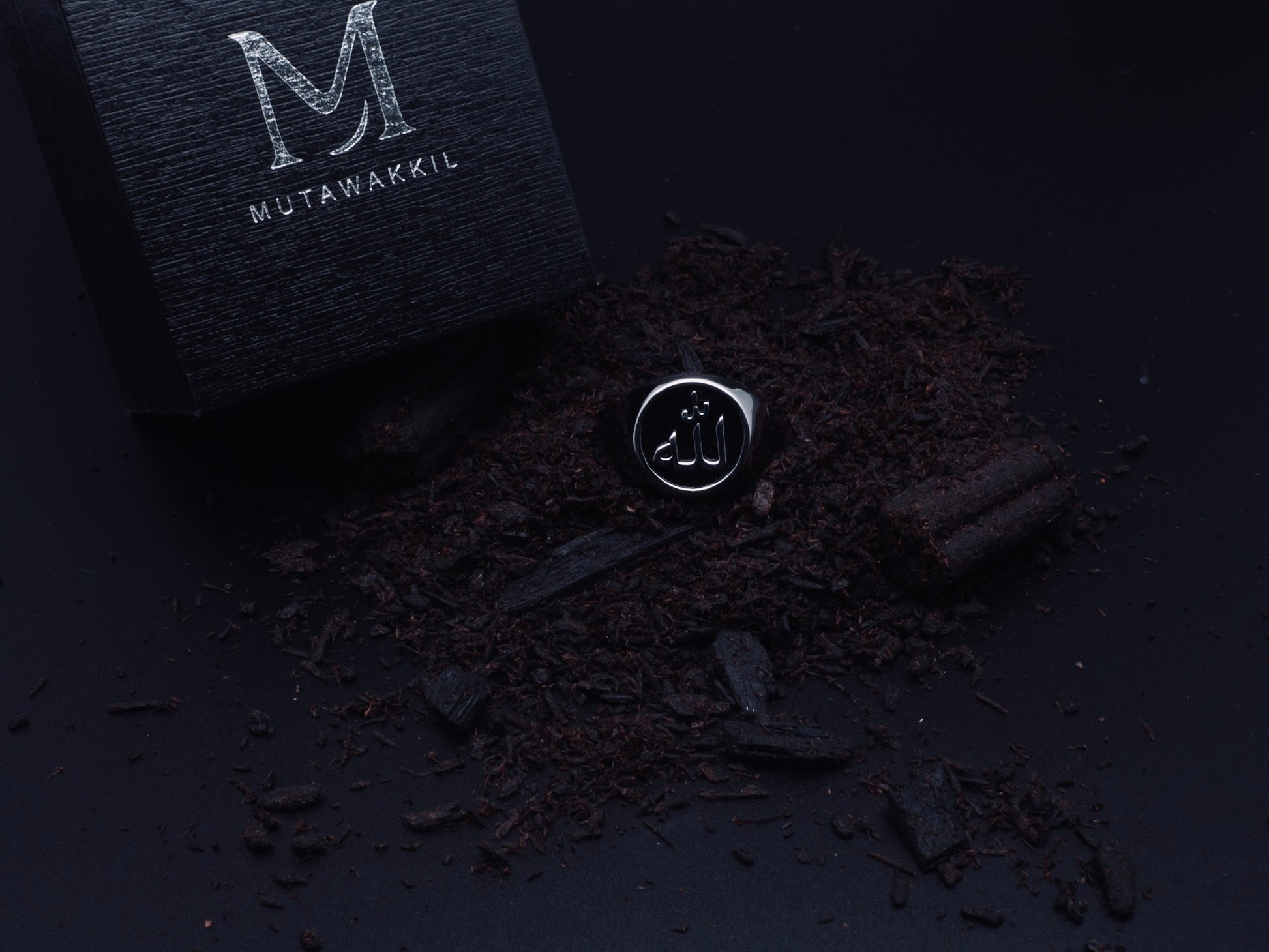Mutawakkil Quwwah black Islamic ring engraved with Allah in Arabic calligraphy, symbol of strength, beside luxury black box.
