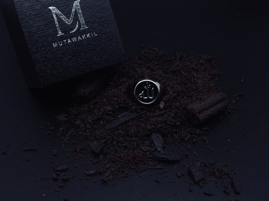 Mutawakkil Quwwah black Islamic ring engraved with Allah in Arabic calligraphy, symbol of strength, beside luxury black box.