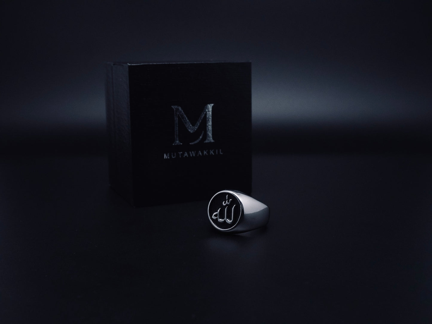 Mutawakkil Quwwah black Islamic ring engraved with Allah in Arabic calligraphy, displayed beside luxury black Mutawakkil box