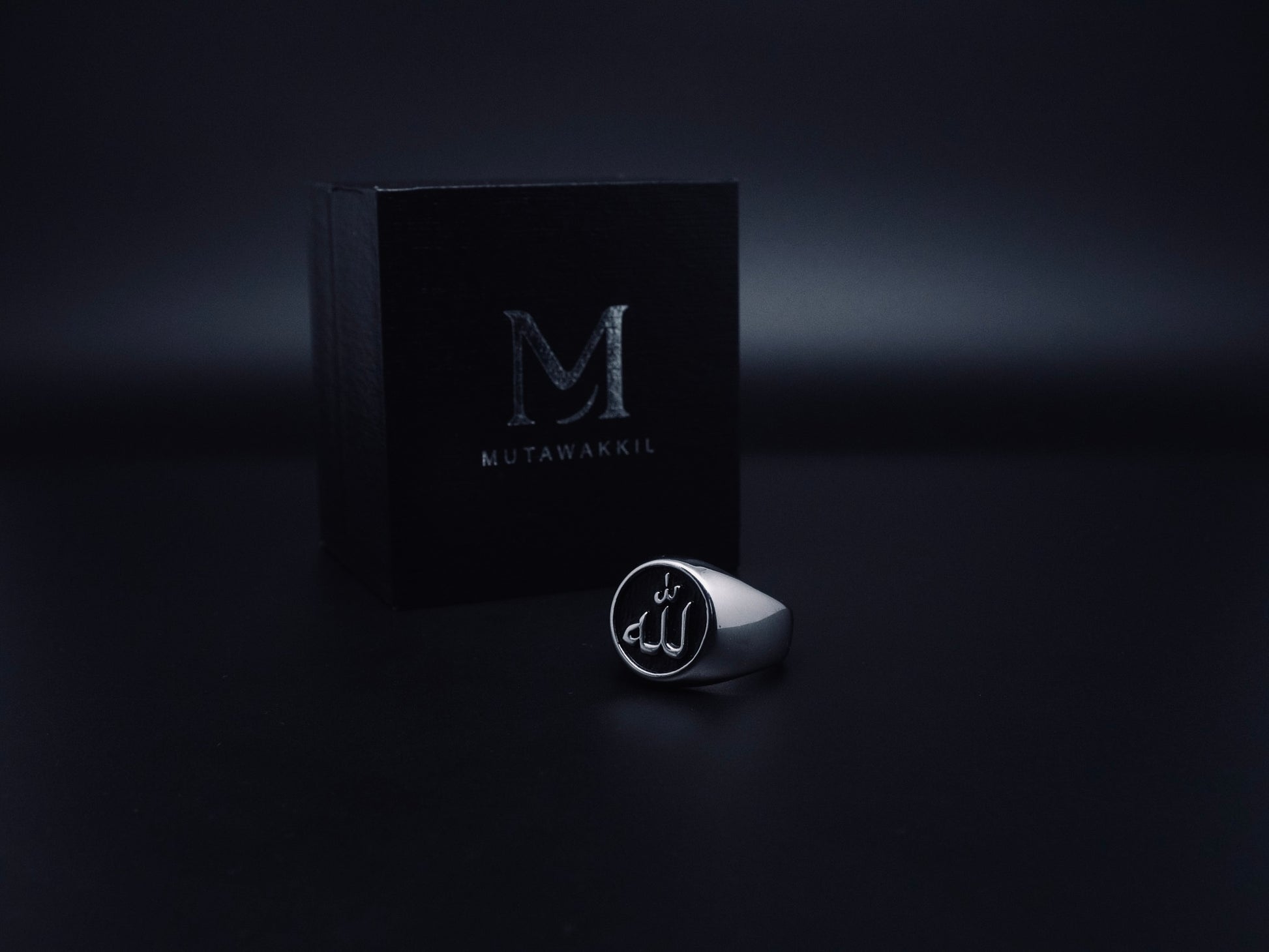 Mutawakkil Quwwah black Islamic ring engraved with Allah in Arabic calligraphy, displayed beside luxury black Mutawakkil box